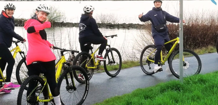 Es sind Schülerinnen und Schüler zu sehen, wie sie auf einem Mountainbike sitzend in die Kamera lächeln.